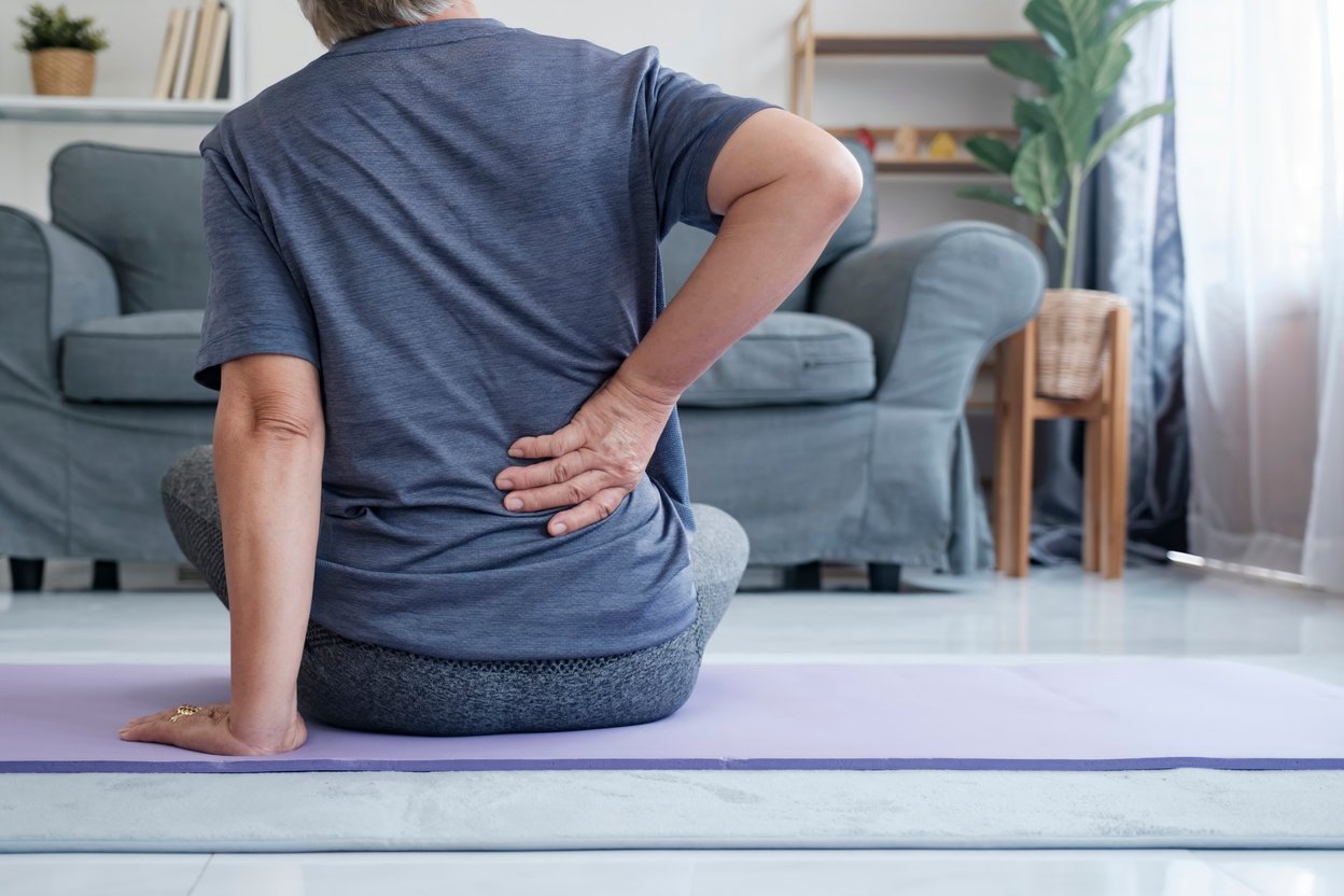 Elderly woman with back pain holding her lower back.